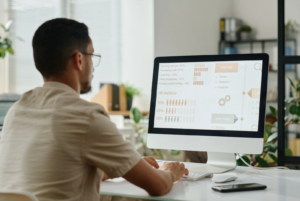 A man sits at a desk looking at a computer monitor with HR data on the screen.