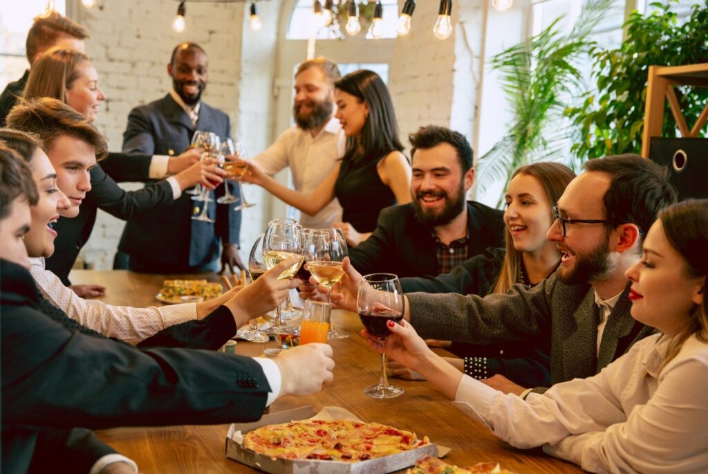 A group of coworkers are at dinner and raise their glasses to cheers together